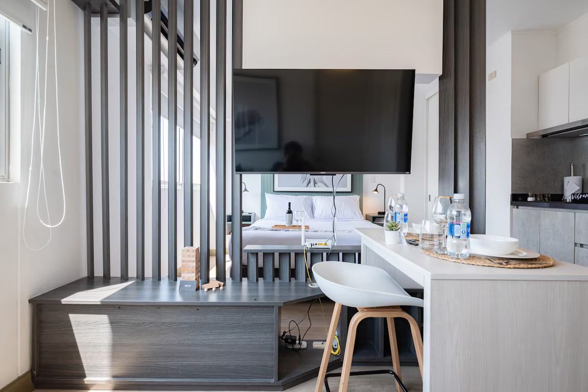 A modern kitchen with a built-in stove, a dining area with a white table and chairs, and a large flat-screen TV mounted above the counter.