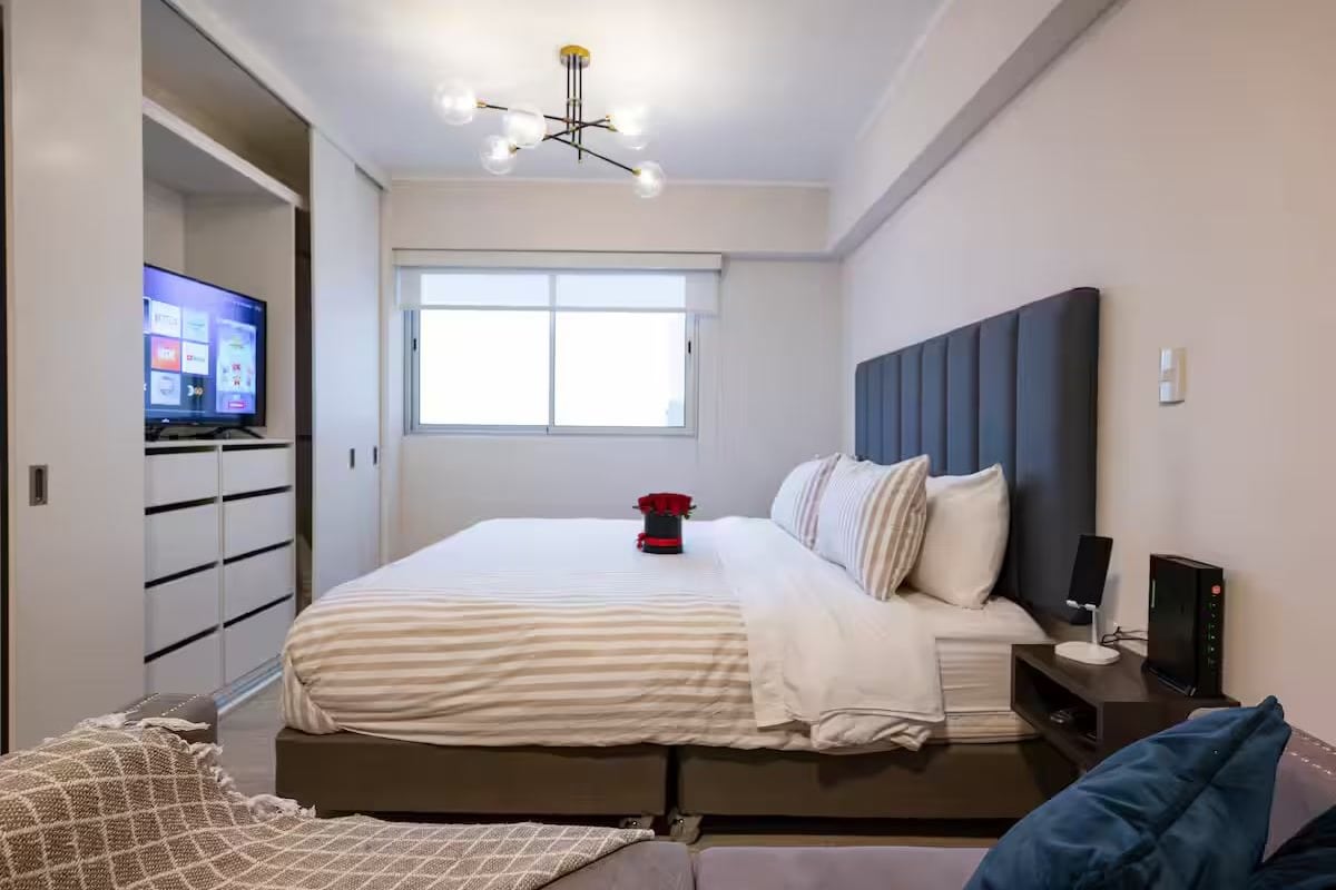 Ein modernes Schlafzimmer mit einem Bett, einem Fernseher, einem Fenster und einem Nachttisch.