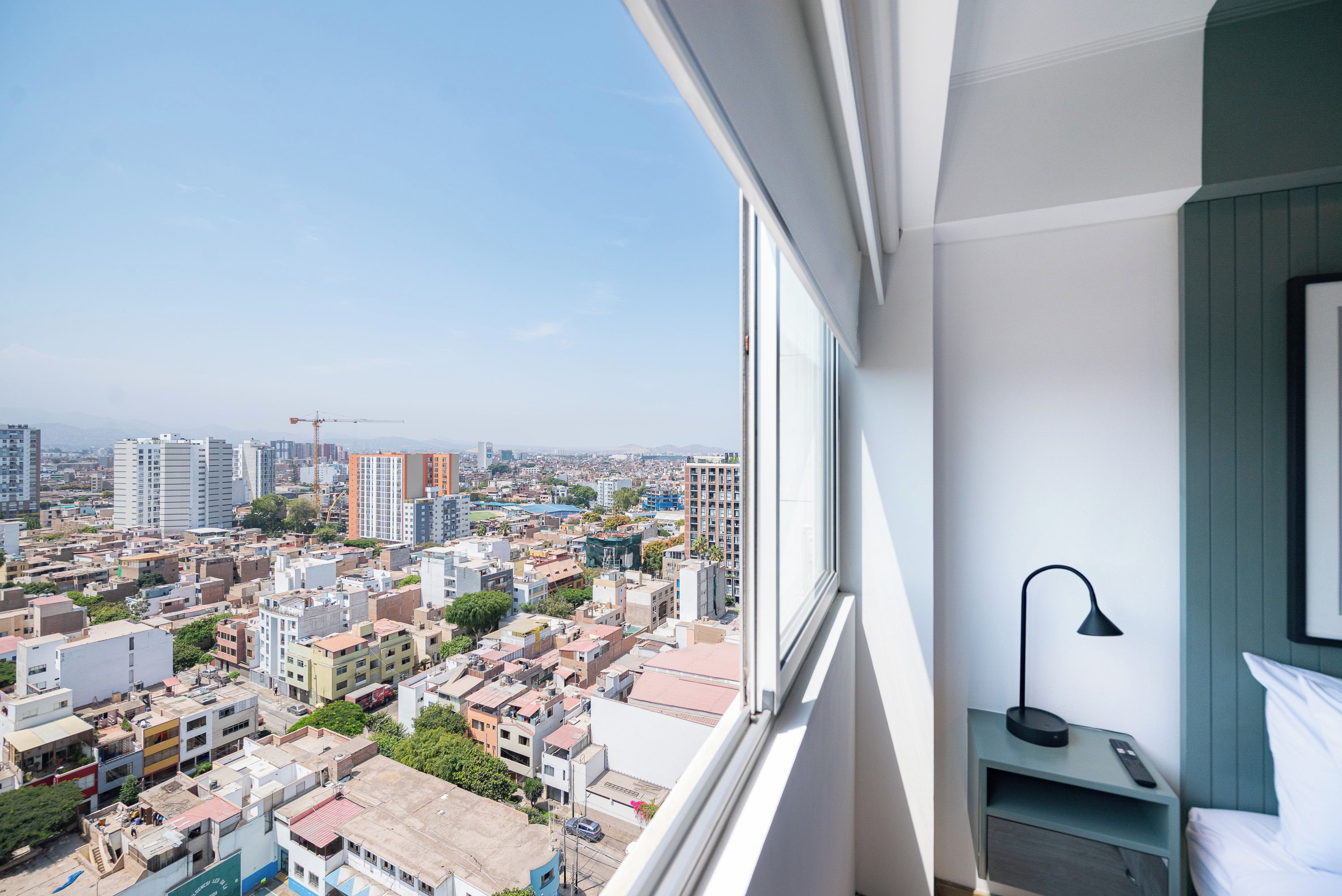 A high-rise apartment with a city view, a bedside table with a lamp, and a bed.