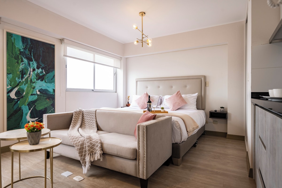 Ein modernes Schlafzimmer mit einem Bett, Nachttischen, einer Couch, einem kleinen Tisch und einem Gemälde.