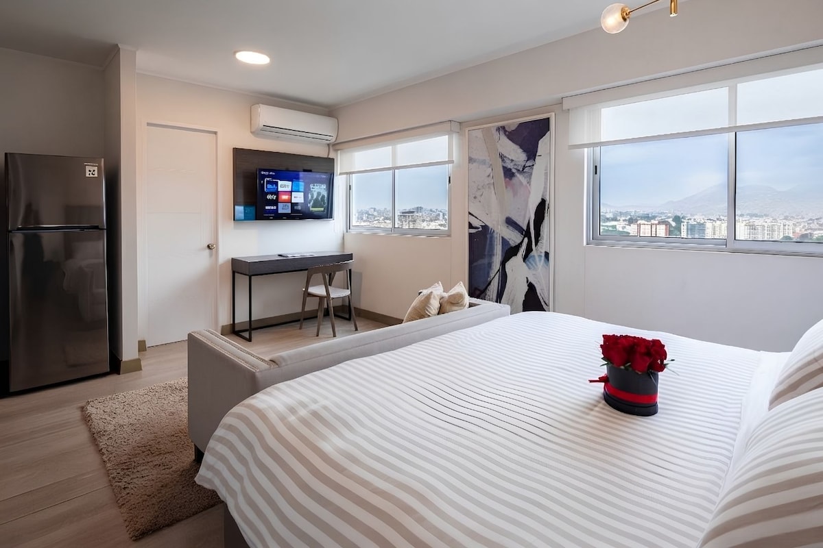 Ein modernes Hotelzimmer mit Bett, Schreibtisch, Fernseher und Blick auf die Stadt.