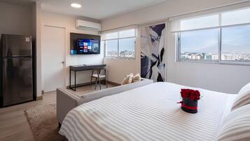 Habitación de hotel moderna con cama, escritorio, televisor y vista a la ciudad.