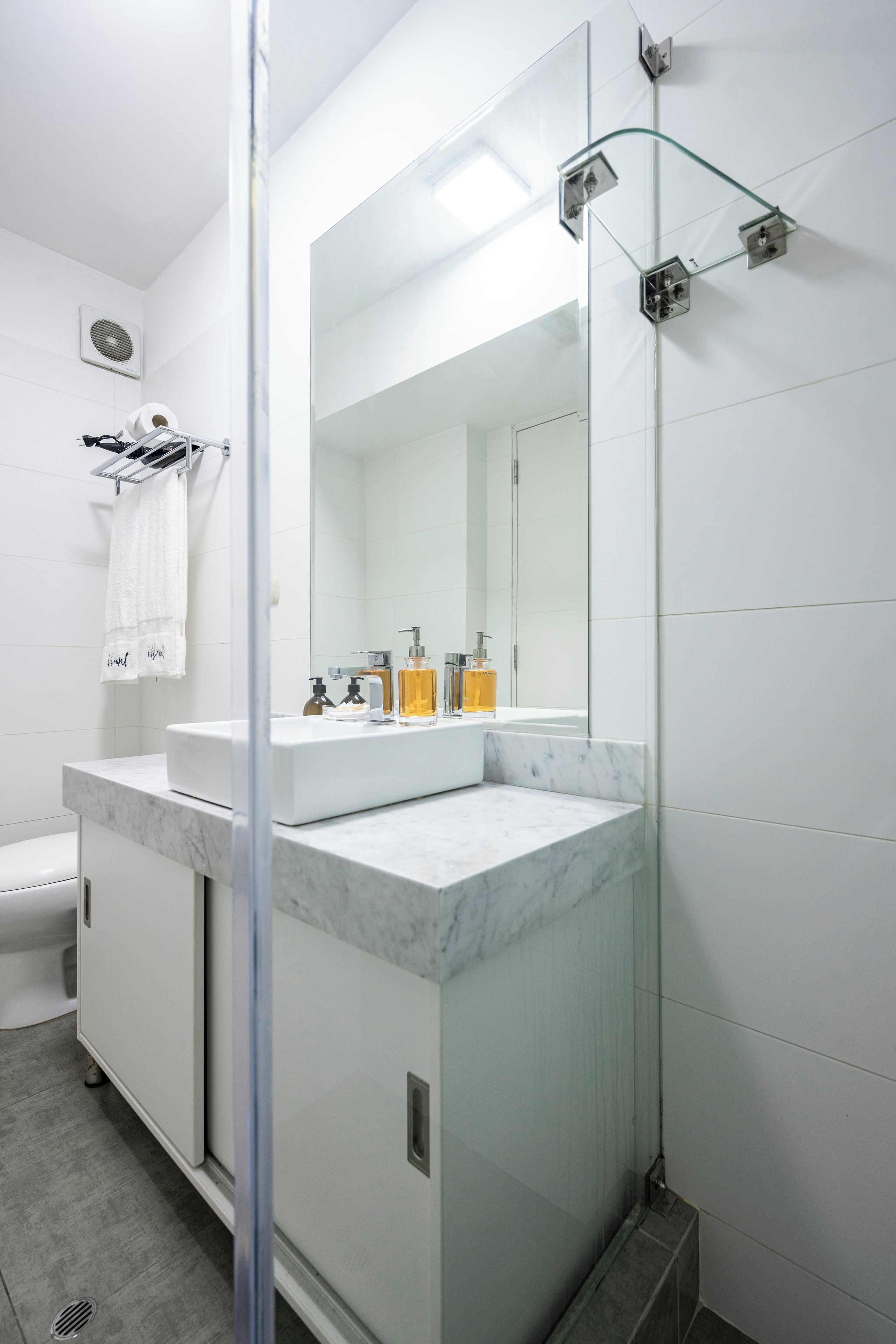 Un baño moderno con cabina de ducha de vidrio, tocador blanco con encimera de mármol y un espejo grande.