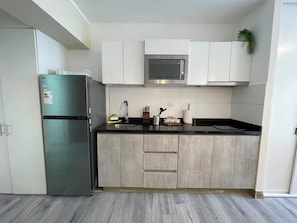 A modern kitchen with a stainless steel refrigerator, a microwave, and wooden cabinets. - Connect Studios by Vibrant (Barranco)