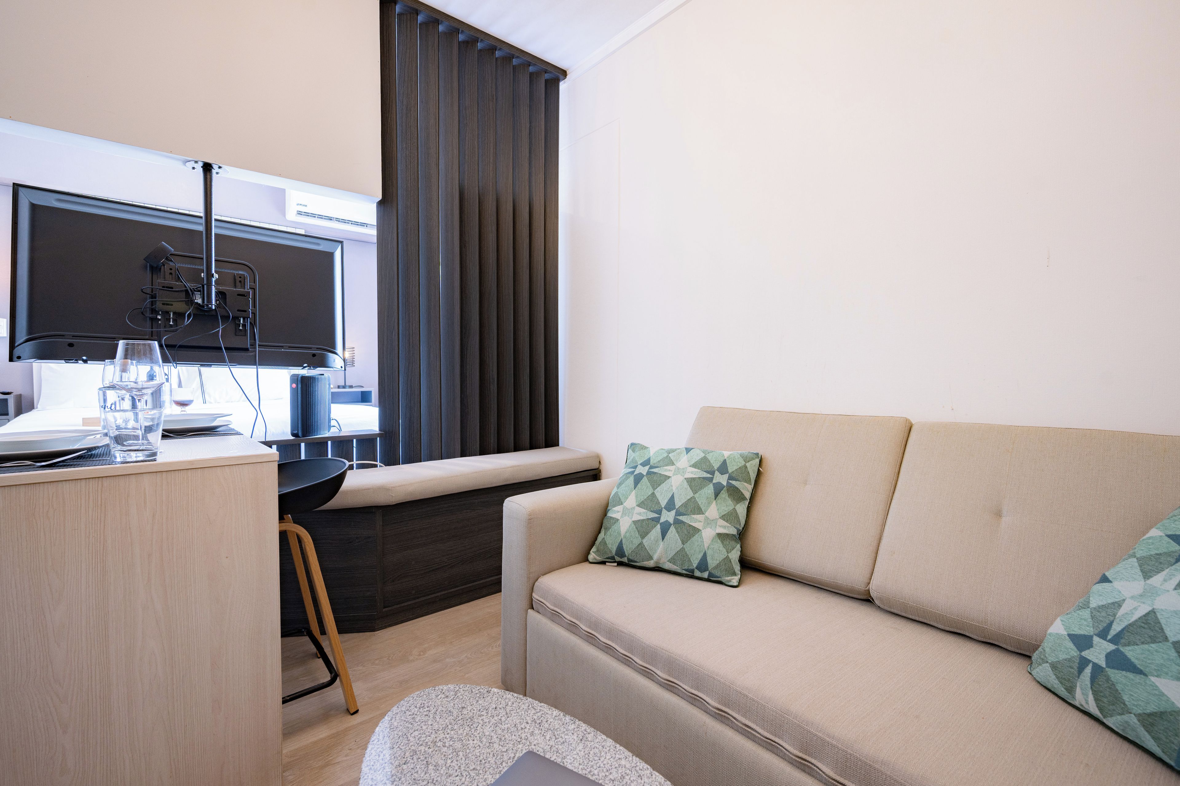 Una sala de estar moderna con un televisor de pantalla plana, un sofá con cojines estampados, un escritorio de madera y una ventana con cortinas.