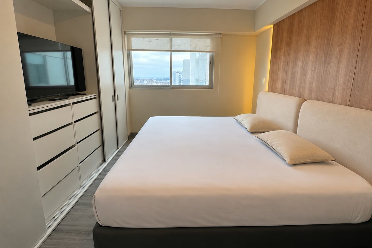 Ein modernes Schlafzimmer mit einem großen Bett, einem Fernseher und einem Kleiderschrank.