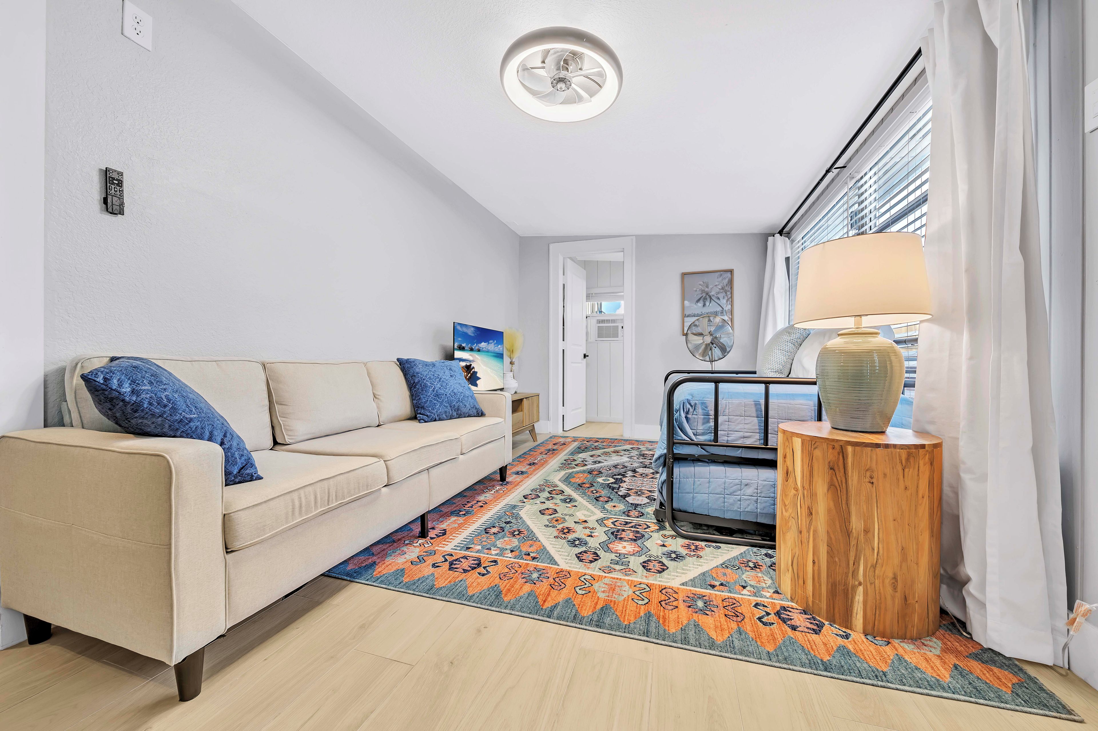 Una sala moderna con un sofá color beige, un tapete estampado y una mesita de madera con una lámpara.
