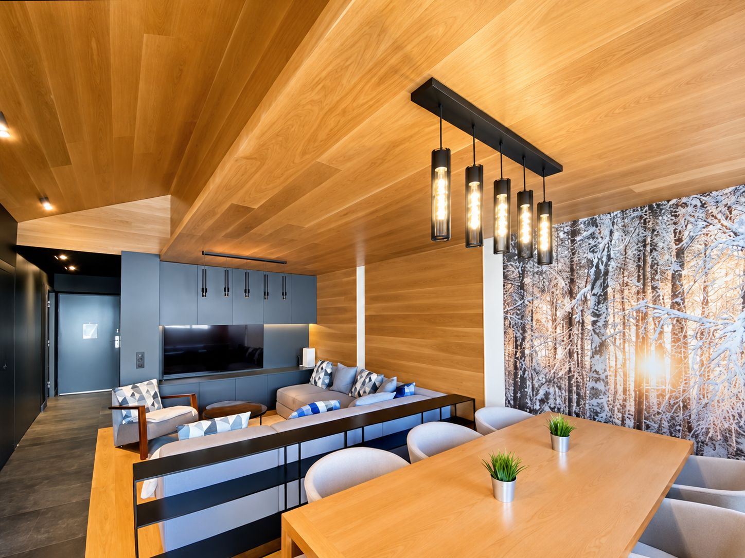 Un intérieur moderne avec un plafond en bois, un coin cuisine et un espace salon avec une table.
