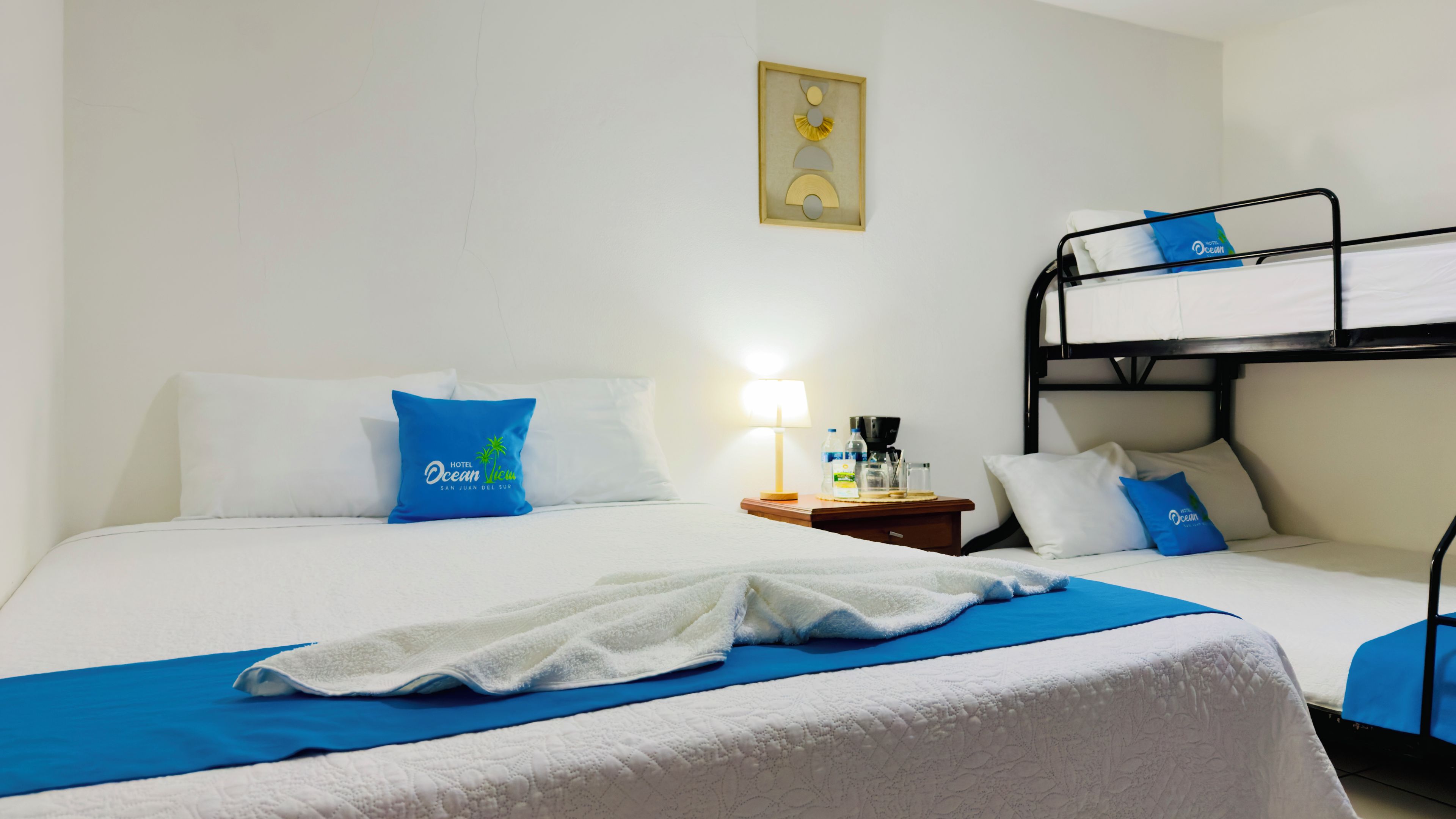 Una habitación de hotel con una cama litera, una mesita de noche con lámpara y una almohada con el logotipo del hotel.