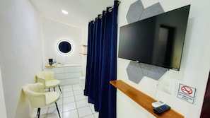 Una habitación moderna con televisión de pantalla plana, un cartel de prohibido fumar, un espejo redondo y una zona de estar con sillones.