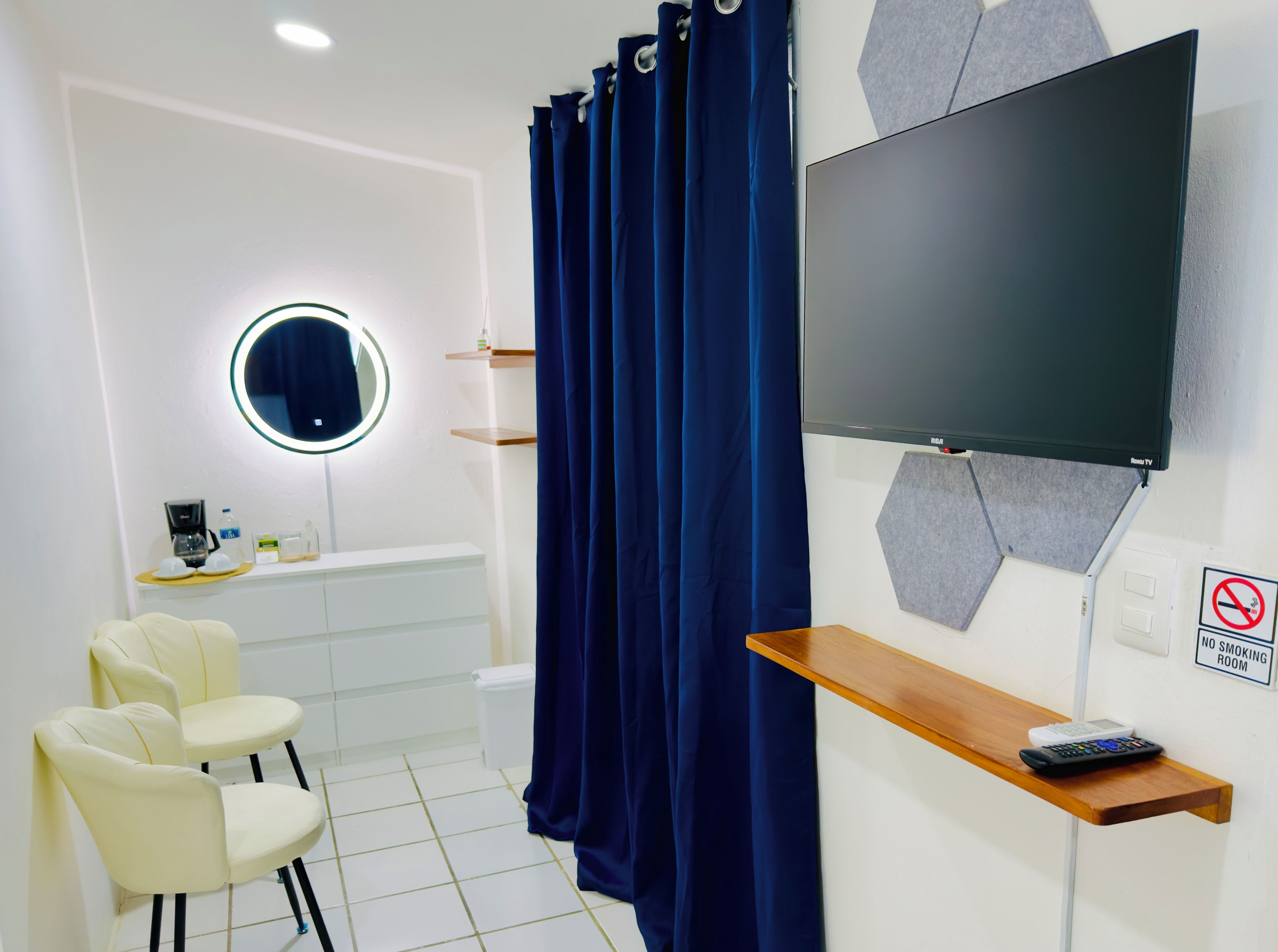 Un baño con cortina de ducha, espejo, inodoro, lavabo, cafetera y televisor montado en la pared.