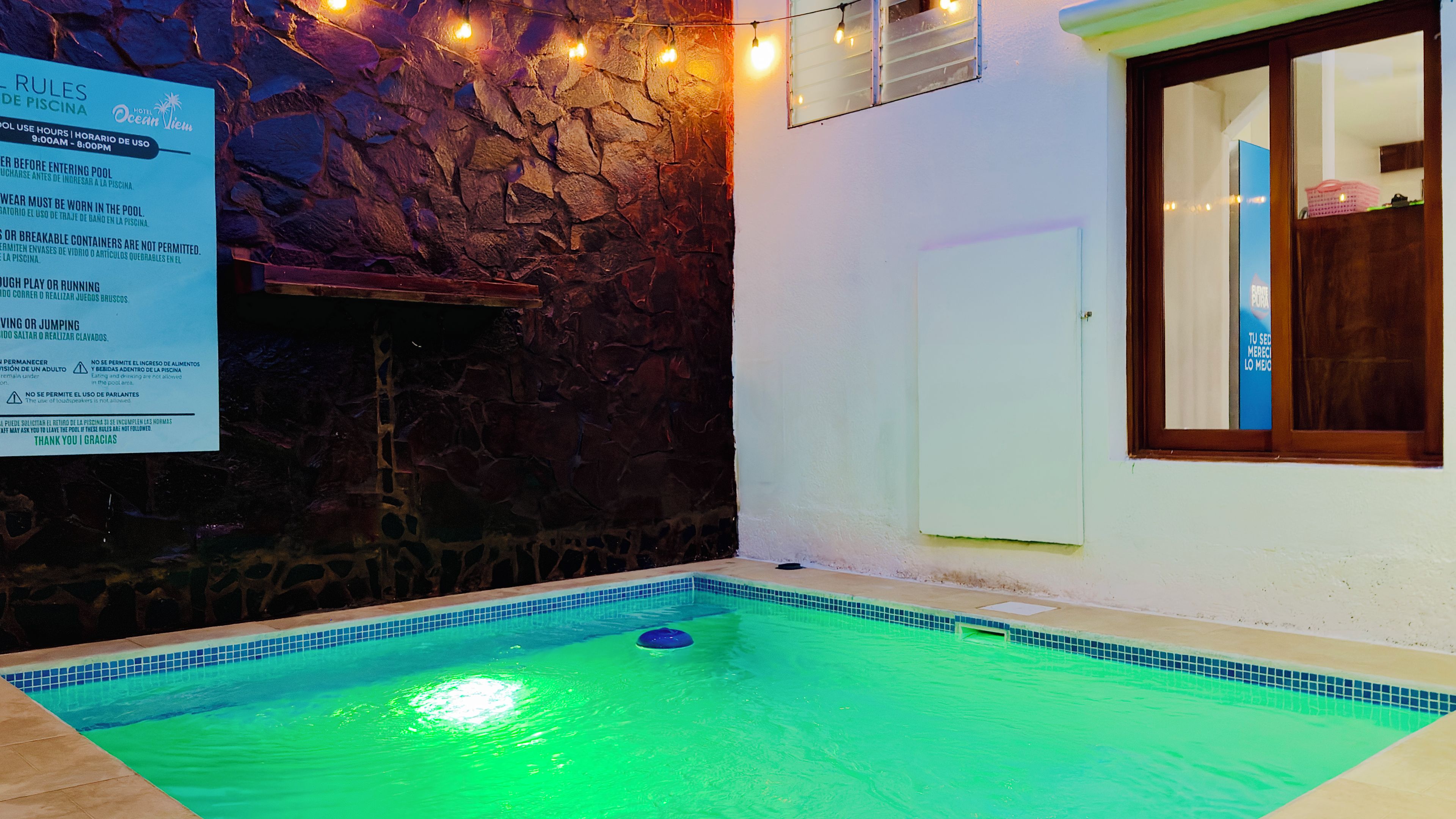 Una piscina amb una paret de pedra i un cartell que enumera les normes de la piscina.