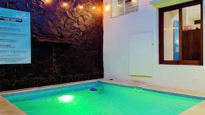 Una piscina con un muro de piedra y un cartel que enumera las normas de la piscina.