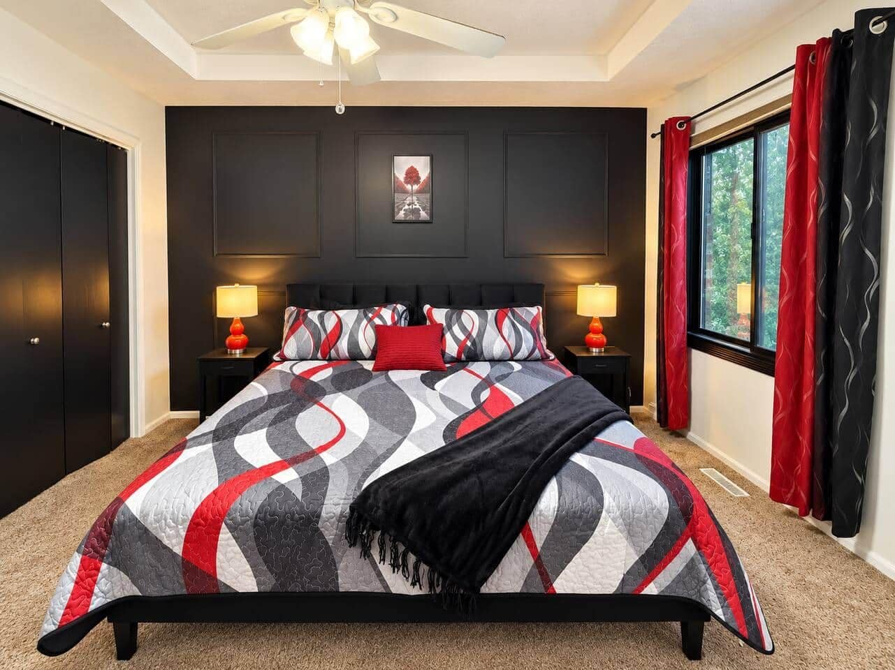 A bedroom with a bed, two bedside tables, a ceiling fan, a window with curtains, and a framed picture on the wall.