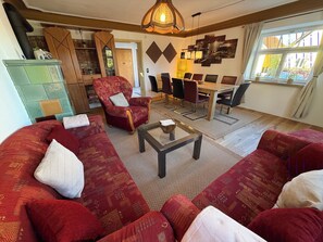 A living room with a sectional sofa, a wooden dining table with chairs, a decorative wall, and a window with curtains. - Landhaus Ziemetshausen – 10 Schlafzimmer, Garten und Platz für 20 Personen (Ziemetshausen)