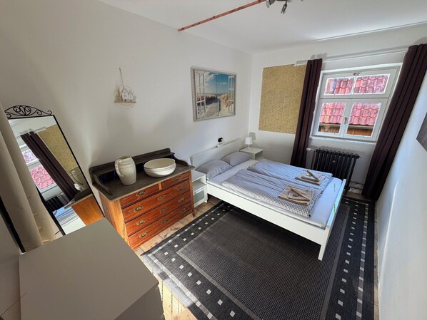 A bedroom with a bed, dresser, bedside table, window, and a view of a building outside. - Landhaus Ziemetshausen – 10 Schlafzimmer, Garten und Platz für 20 Personen (Ziemetshausen)