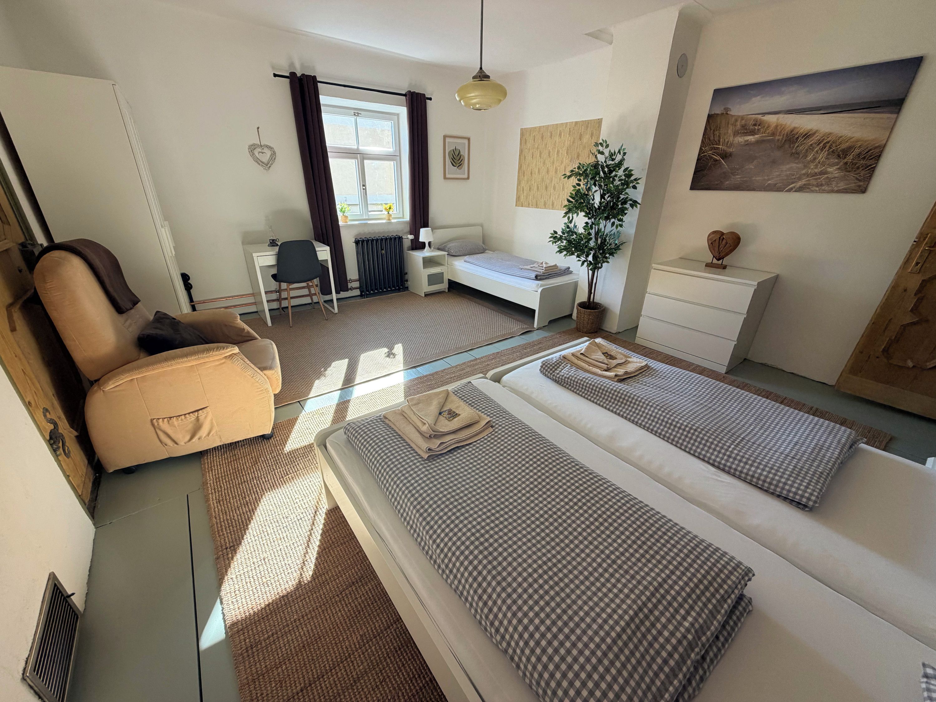 Een slaapkamer met een bed, een bureau, een stoel, een kamerplant en een schilderij aan de muur.