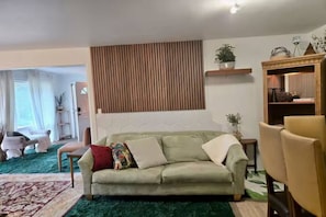 Ein Wohnzimmer mit einer Couch, einem grünen Teppich, einer Wand aus Holzleisten und einer kleinen Pflanze auf einem Regal.
