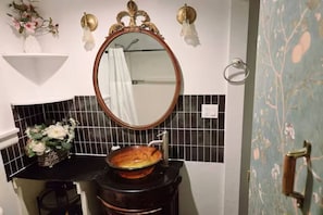 Et badeværelse med et rundt spejl, sort flisebeklædt væg og en vask i træ.