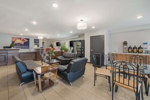 Ein modernes Wohnzimmer mit einer Couch, einem Esstisch mit Stühlen und einer Küchenzeile inklusive Kühlschrank und Kaffeemaschine.