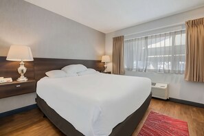 Ein Hotelzimmer mit einem großen Bett, zwei Nachttischen mit Lampen, einem Fenster mit Vorhängen und einem roten Teppich.