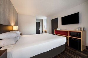 Ein Hotelzimmer mit einem großen Bett, einem Flachbildfernseher, einer Mikrowelle und einer kleinen Küchenzeile.