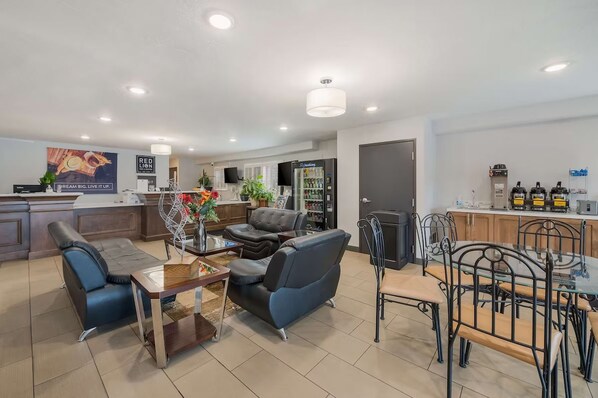 Ein modernes Wohnzimmer mit einer Couch, einem Esstisch mit Stühlen und einer Küchenzeile inklusive Kühlschrank und Kaffeemaschine.