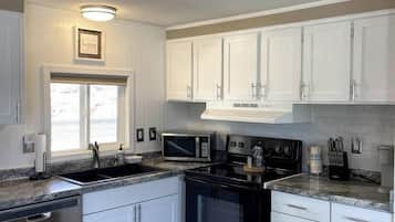 A kitchen with white cabinets, a black stove, a microwave, and a stainless steel dishwasher.