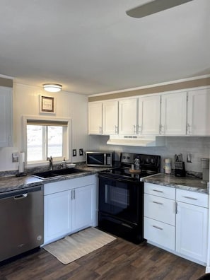 A kitchen with white cabinets, a black stove, a microwave, and a stainless steel dishwasher. - Stunning Parker Home with River Views & Privacy! (Parker)