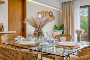 A dining area with a glass table, wicker chairs, white plates, and clear glassware. - Oceanfront 1BR Condo With Pool, Gym, AC, and Balcony (La Cruz de Huanacaxtle)
