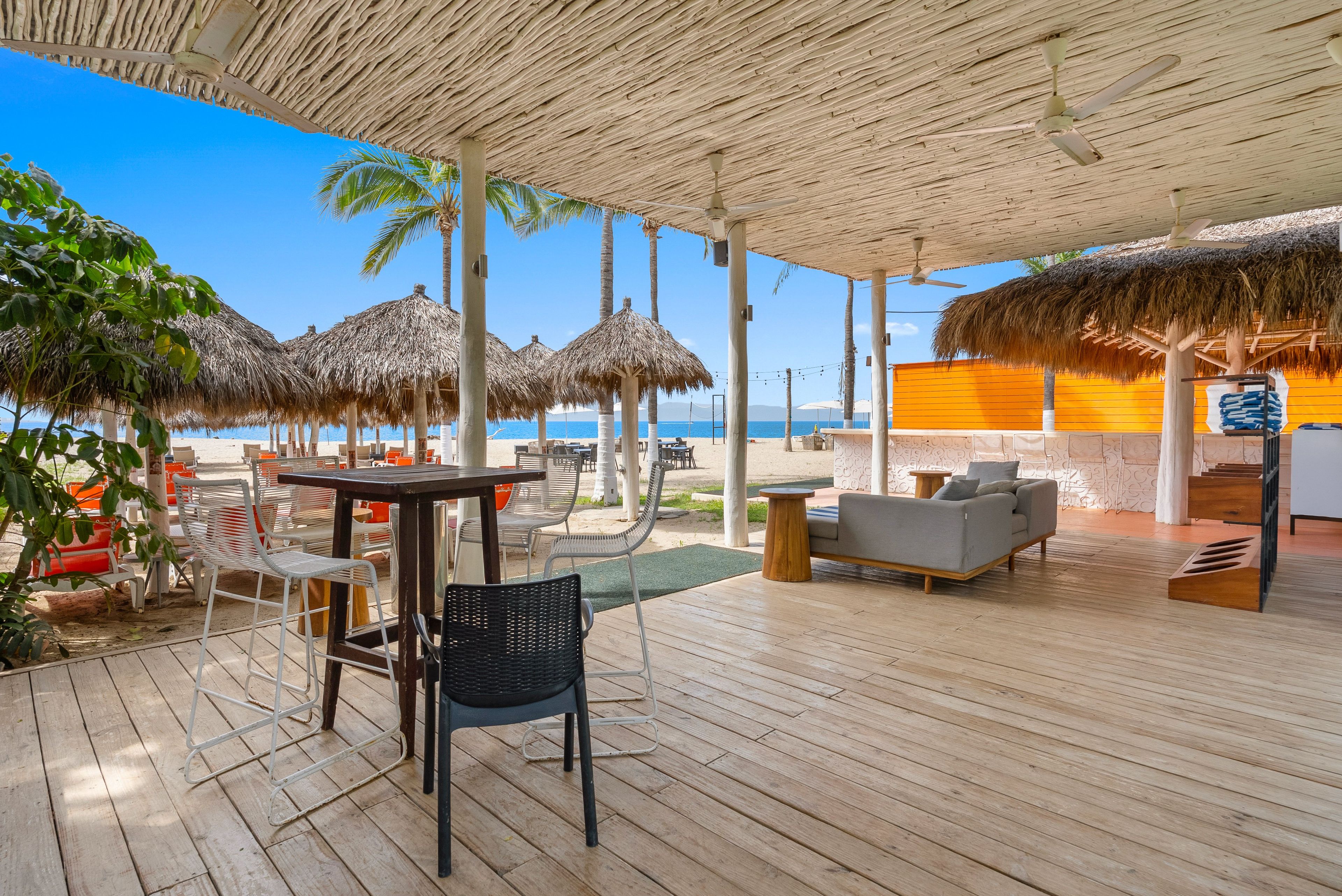 Un espace extérieur aménagé, abrité et doté de tables, de chaises, d’un canapé, et offrant une vue sur la plage et l’océan.