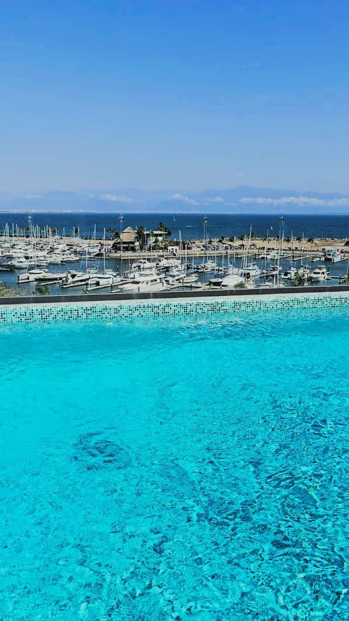 A marina with boats docked, a clear blue pool, and a view of the ocean.