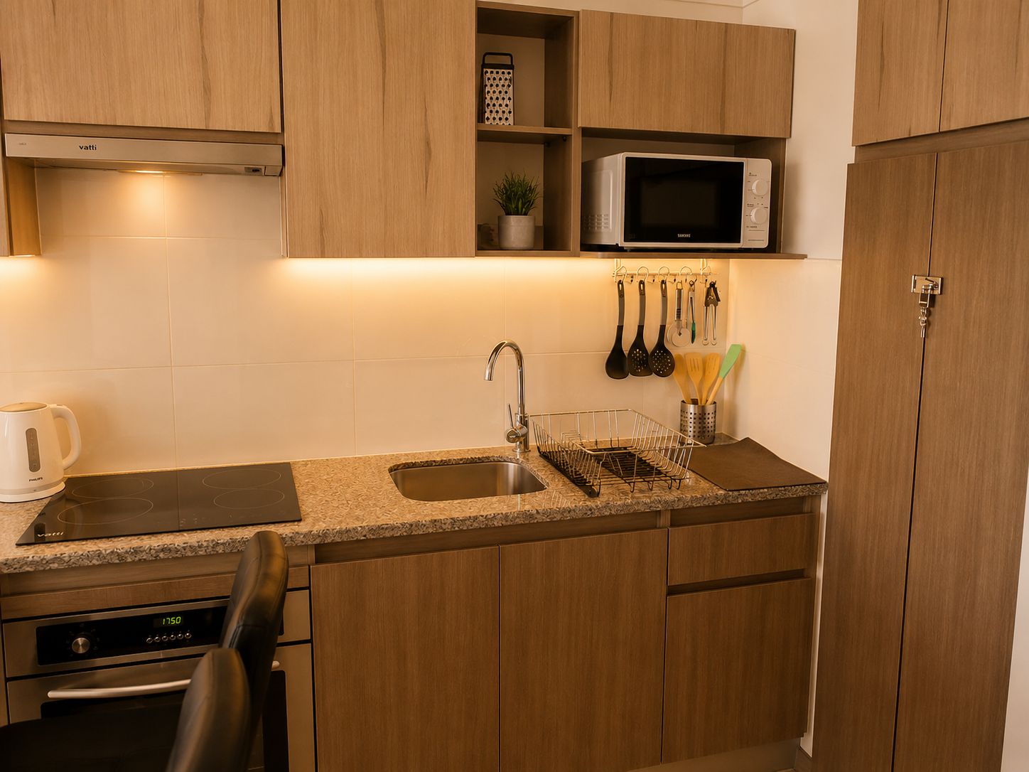 Una cucina compatta con mobili in legno, un forno a microonde, un bollitore e una lavastoviglie.