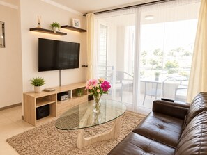 A modern living room with a flat-screen TV, a glass coffee table, a leather sofa, and a view of the outdoors through large sliding doors. - New Listing (Coquimbo)