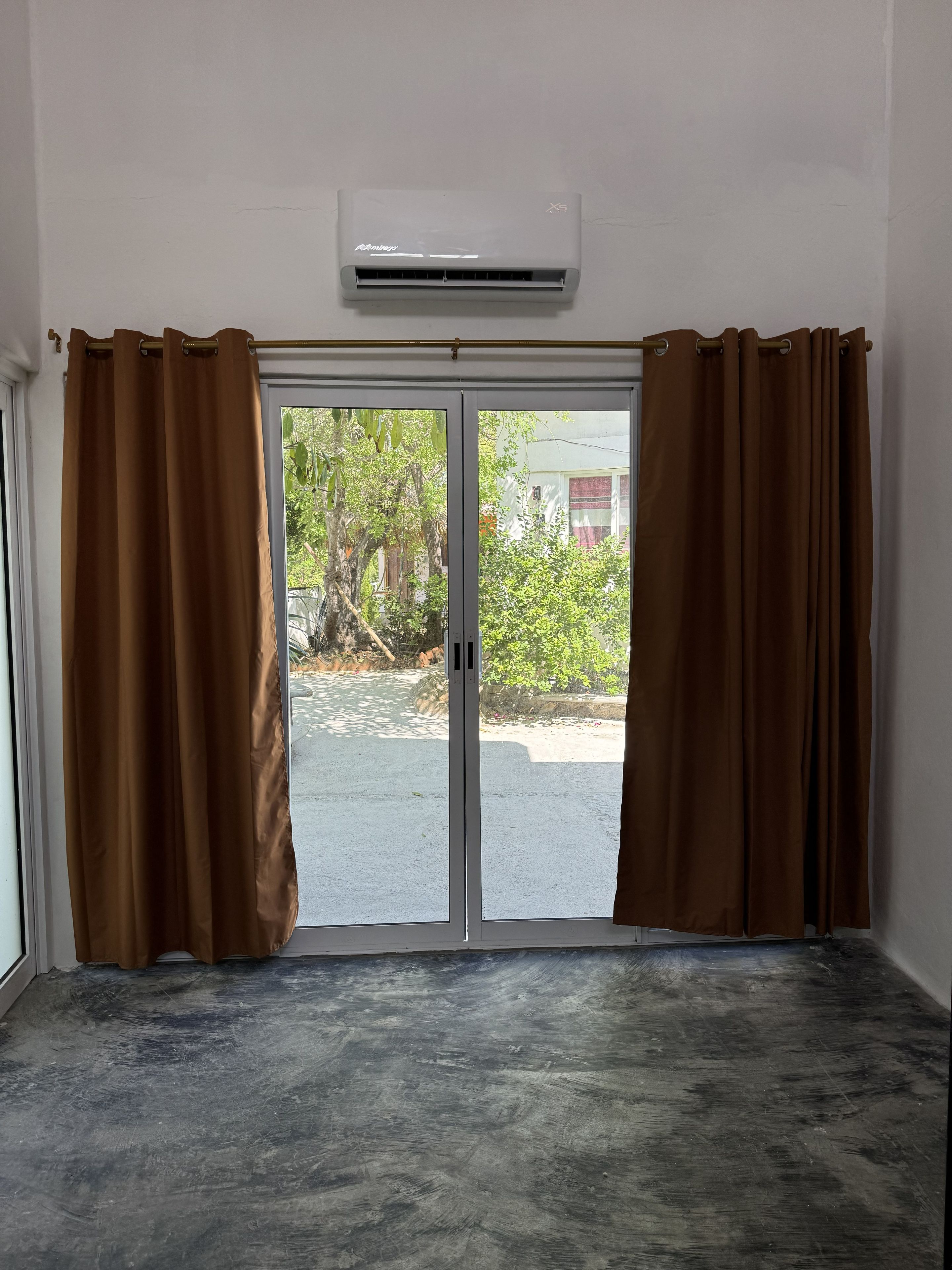 Una habitación con puerta corrediza de vidrio, cortinas marrones y un equipo de aire acondicionado instalado en el techo.