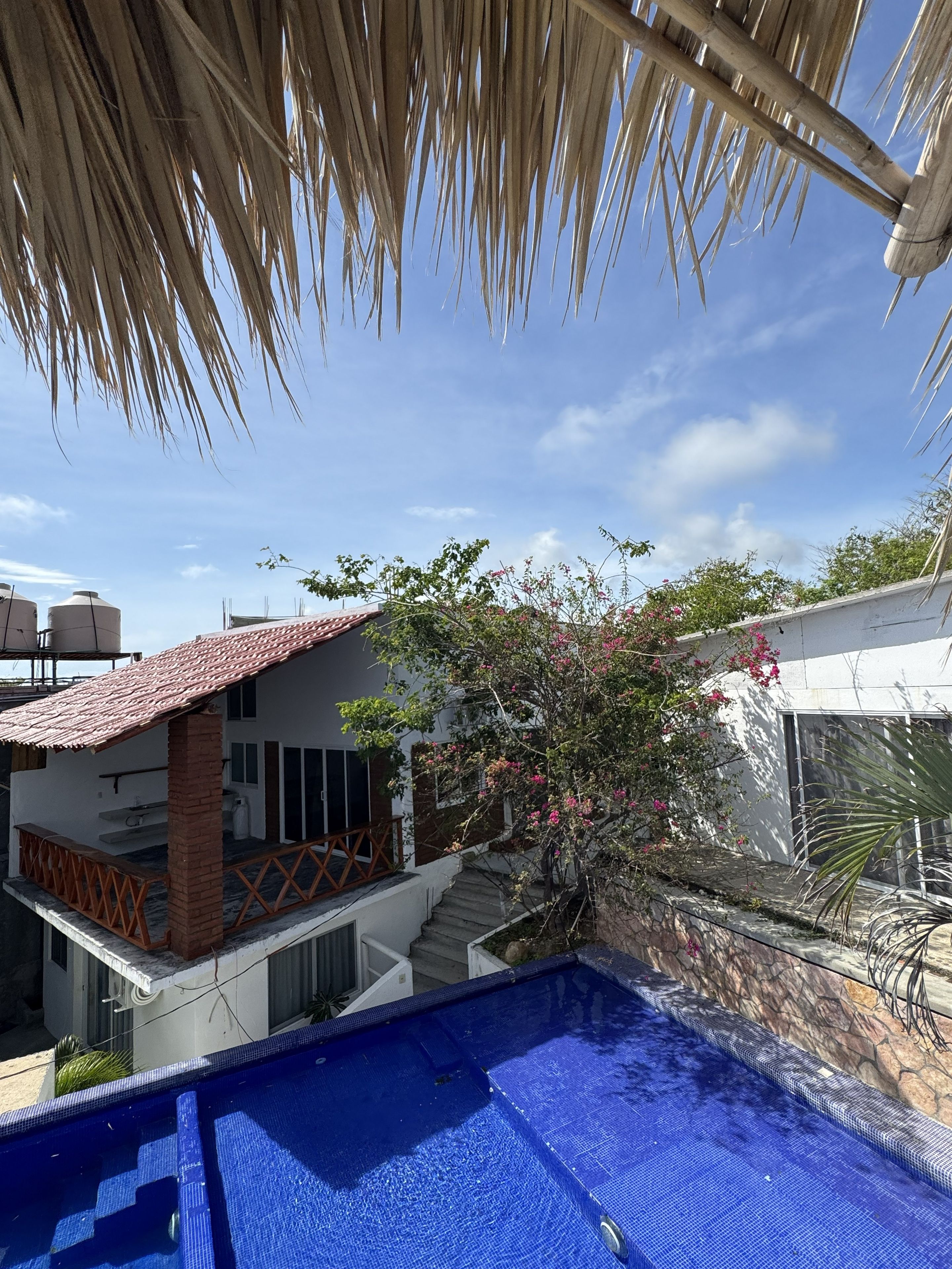Zona residencial con piscina, una casa con techo de tejas y una escalera que lleva a un balcón.