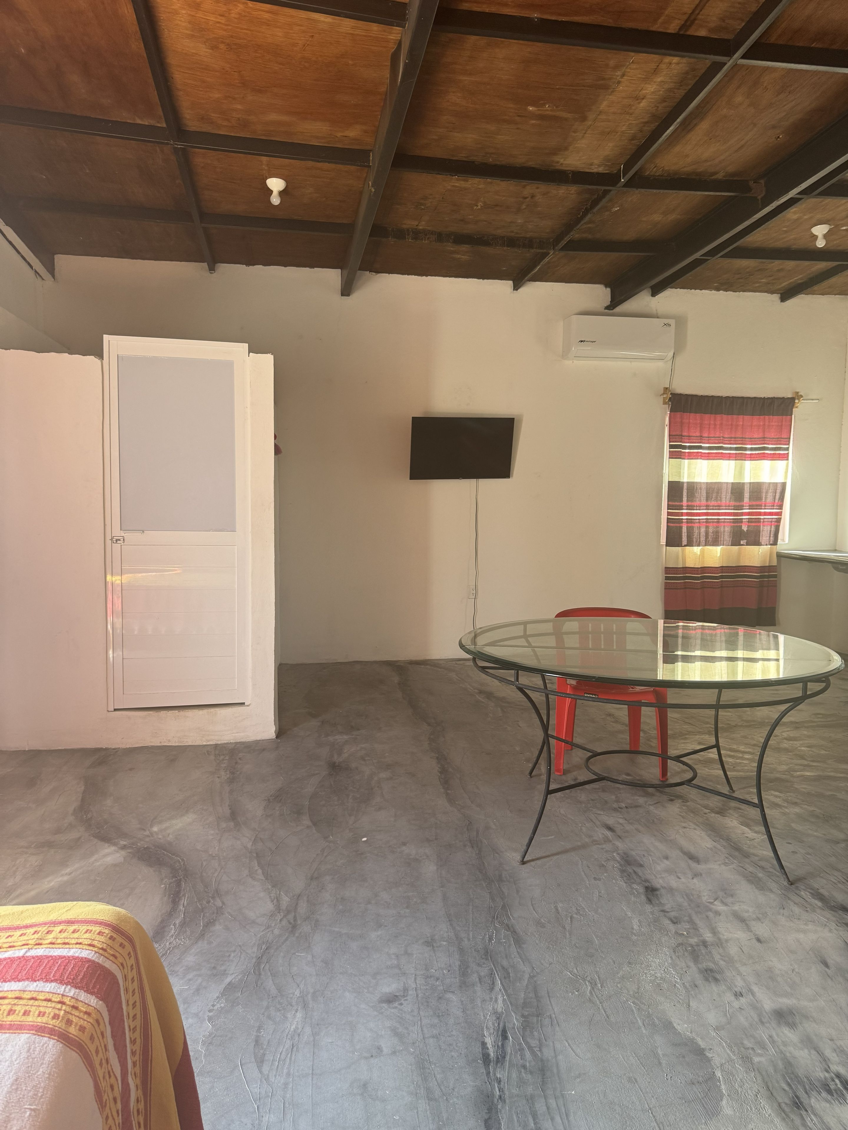 A room with a glass table, red chairs, a white door, and a ceiling fan.