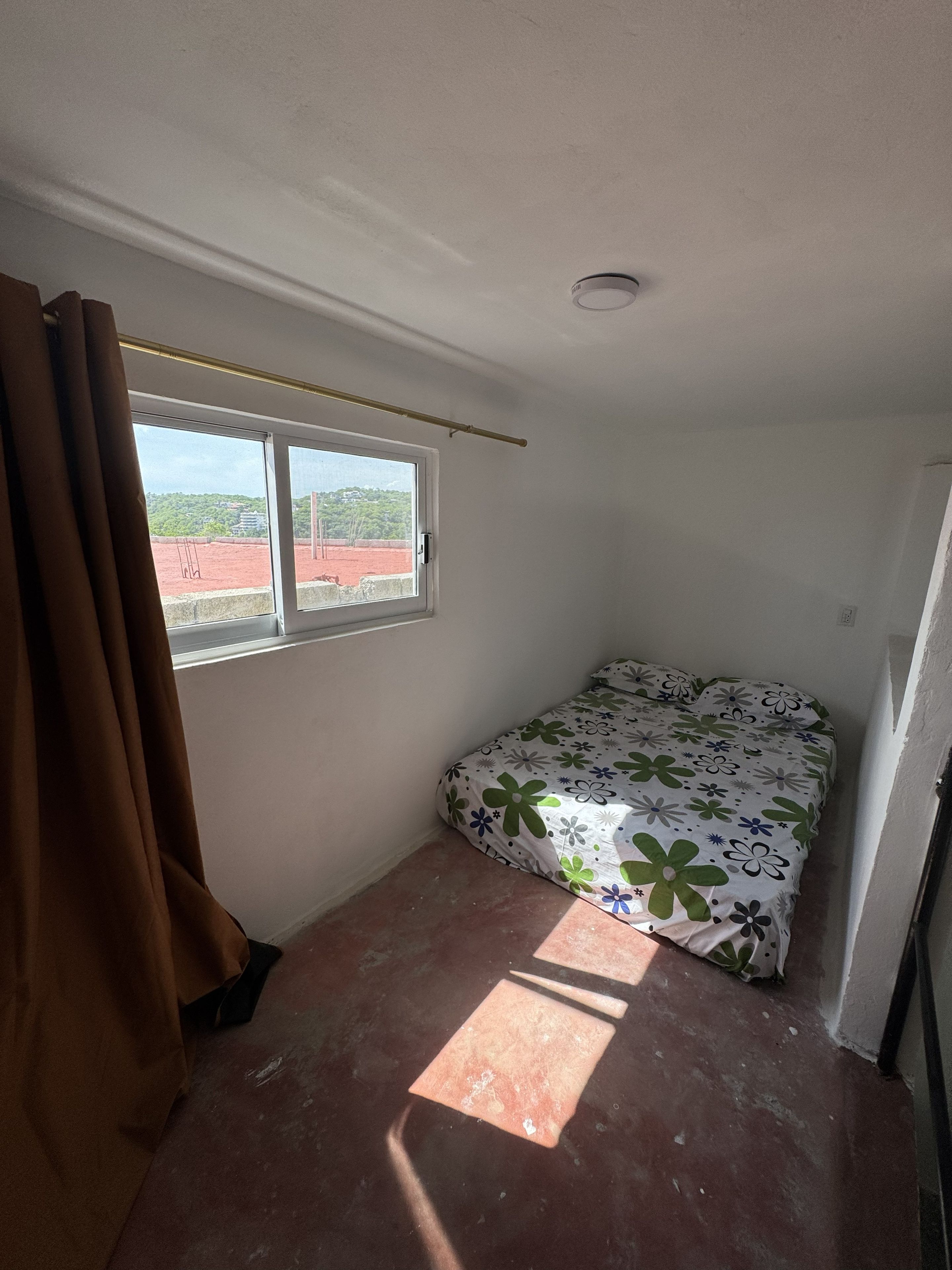 Un dormitorio con cama, ventana y cortina.