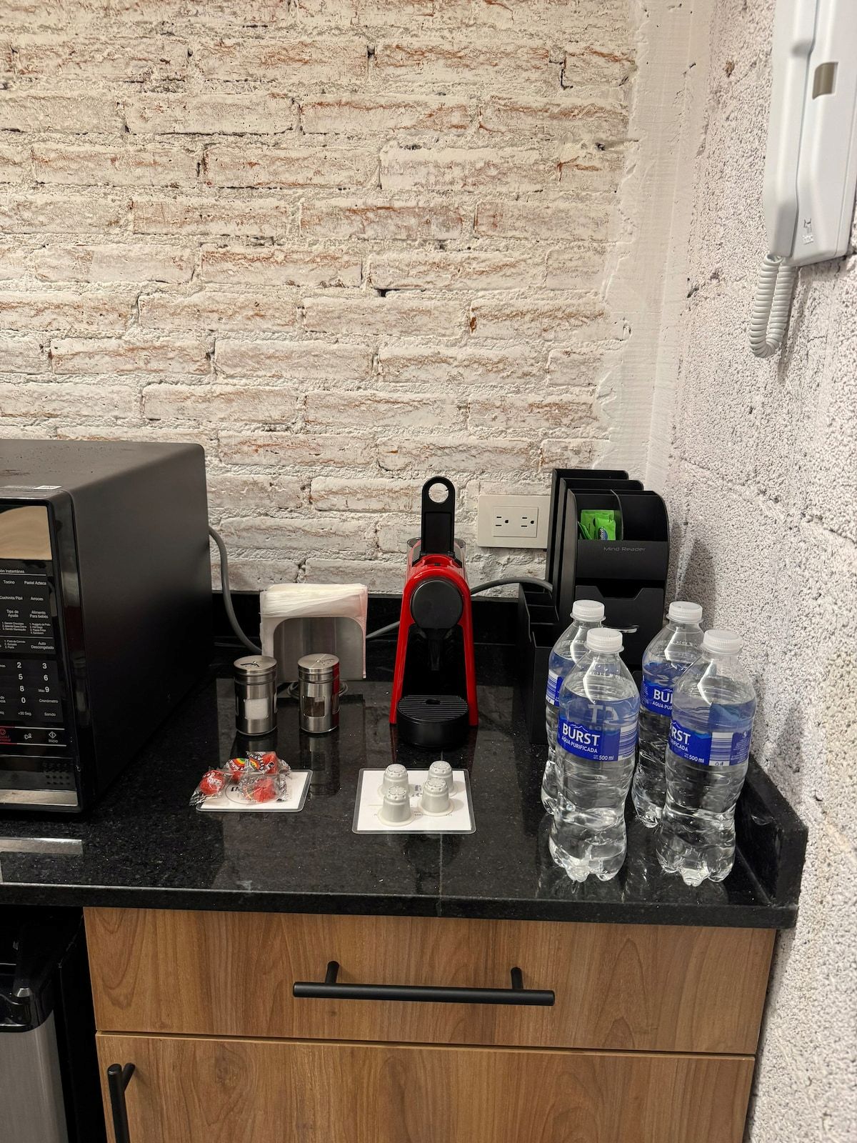 Un piano di lavoro in cucina con una macchina da caffè, un forno a microonde, un bollitore e acqua in bottiglia.