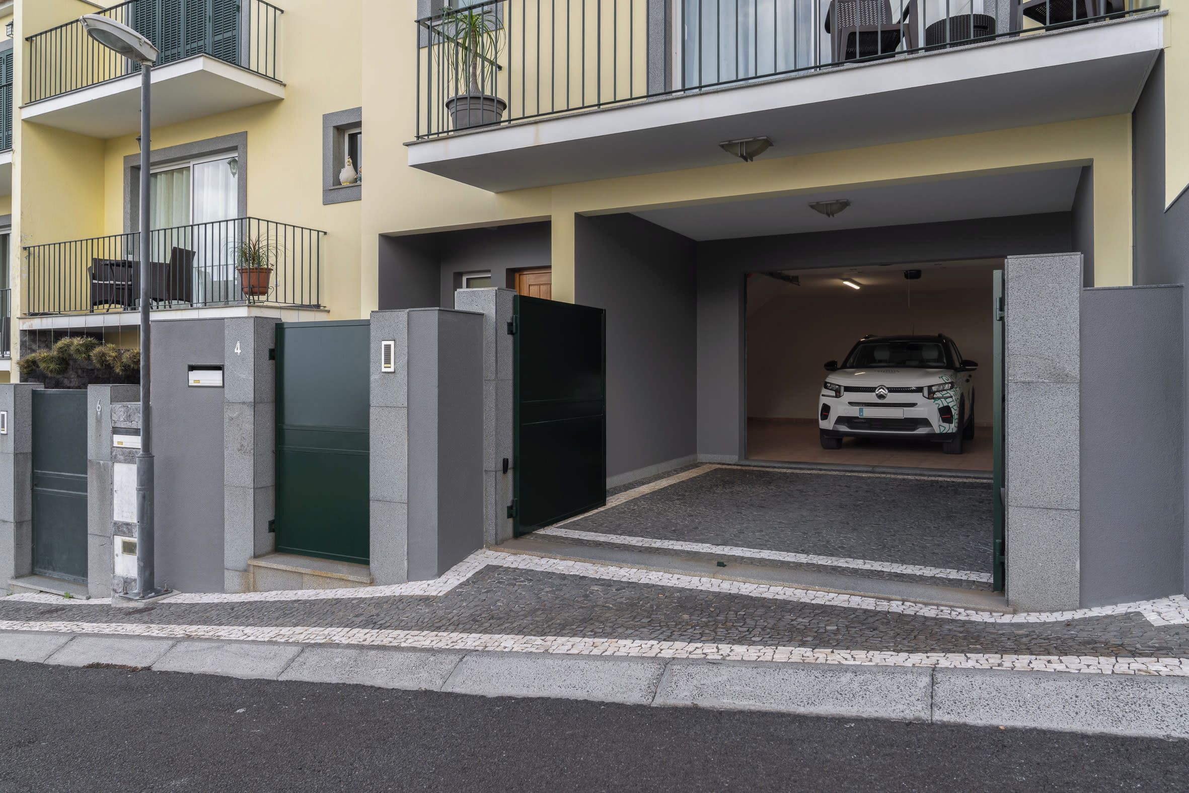 Un edificio de apartamentos moderno con entrada protegida, un coche estacionado en el interior y un balcón con mobiliario exterior.