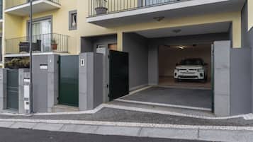 Un edificio de apartamentos moderno con entrada protegida, un coche estacionado en el interior y un balcón con mobiliario exterior.