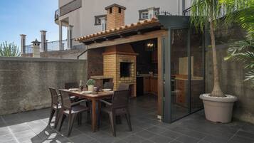 An outdoor patio with a brick oven, dining table, chairs, and a potted plant.