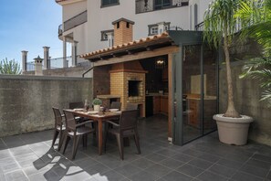 An outdoor patio with a brick oven, dining table, chairs, and a potted plant.