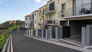 A residential building with balconies, a gated entrance, and a view of a hill with a building in the distance.