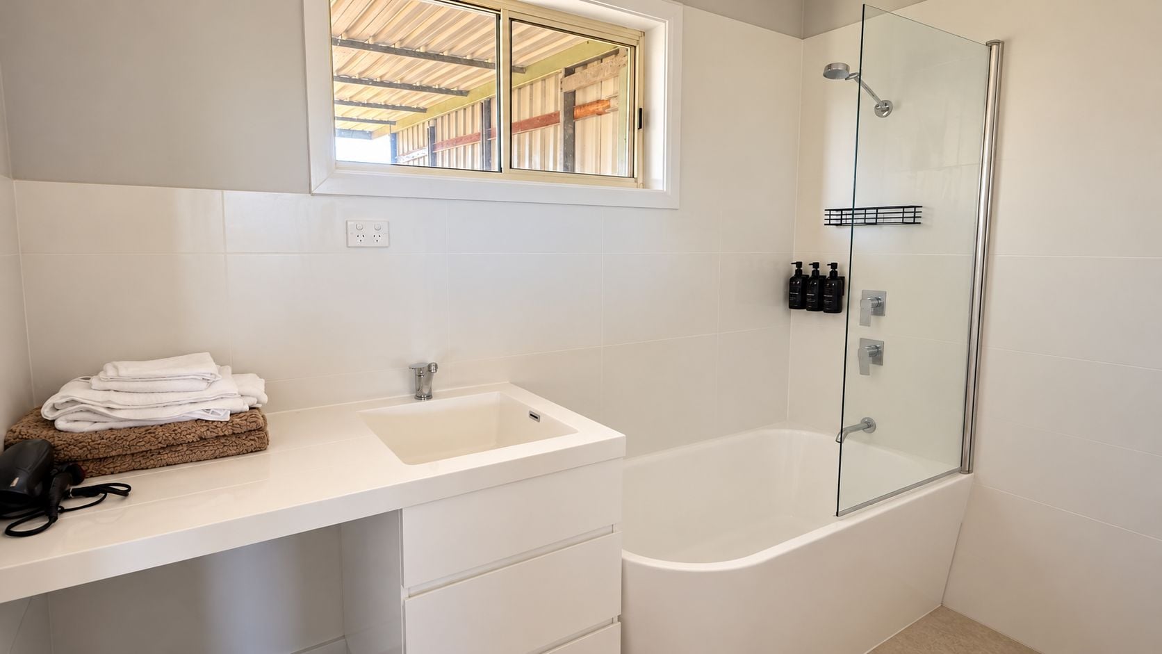A bathroom with a white sink, a glass-enclosed shower, and a window above the sink.