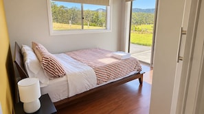 Un letto singolo con struttura in legno, biancheria da letto bianca e cuscini a righe, posizionato vicino a una finestra con vista su un paesaggio verde.