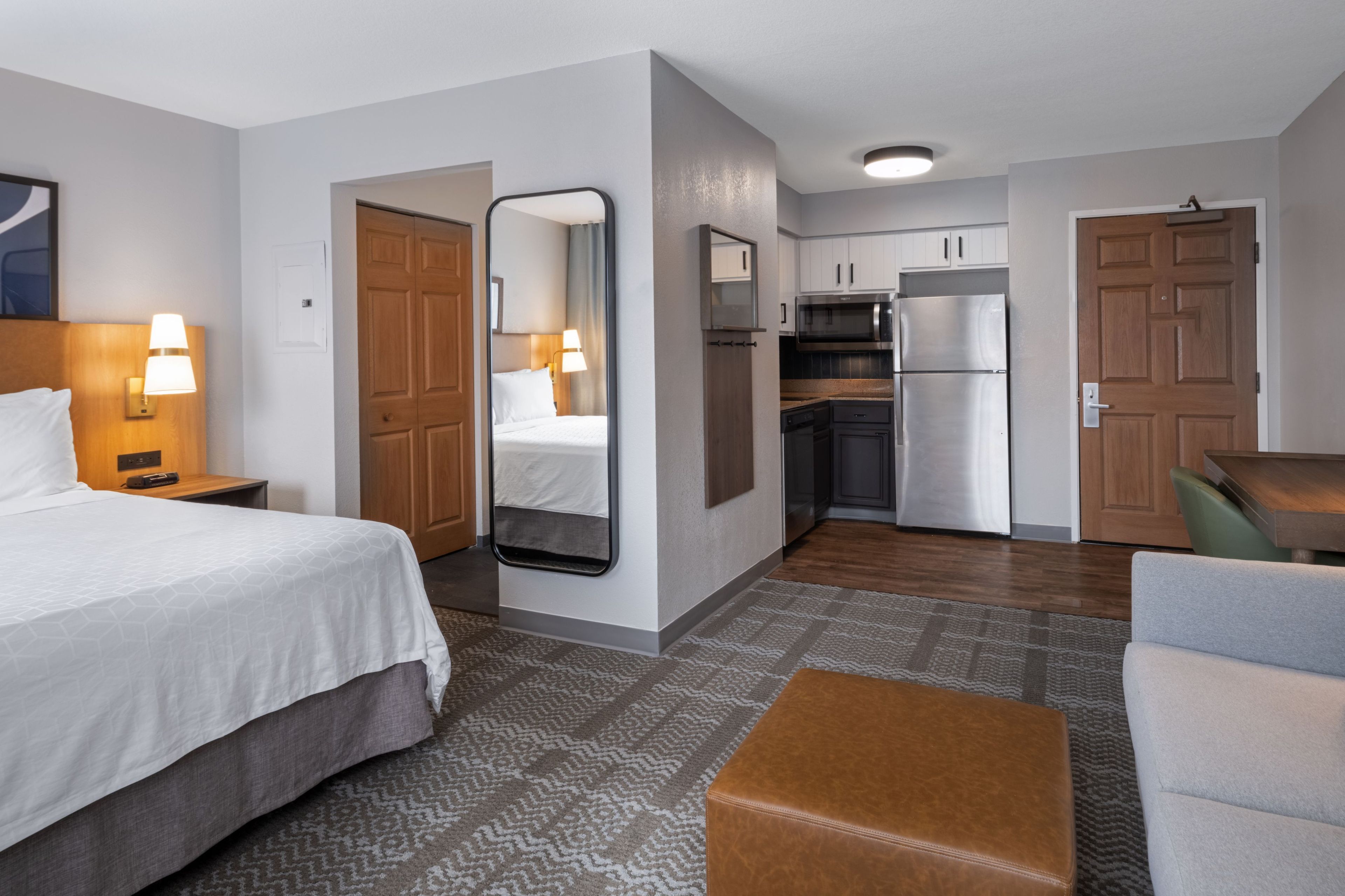 A hotel room with a bed, a sitting area, a kitchenette, and a bathroom.