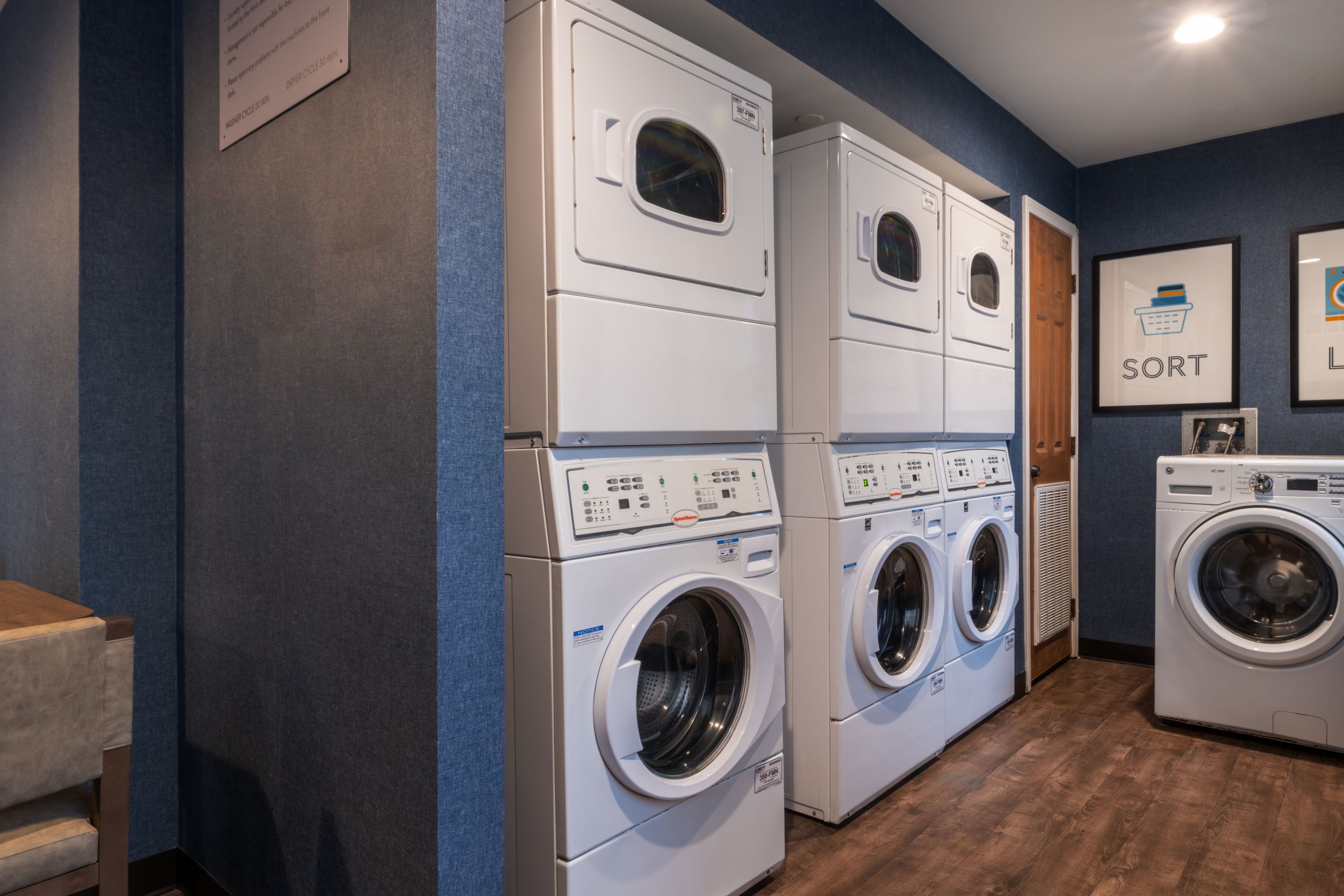 A laundry room with stacked front-loading washers and dryers, wooden flooring, and a blue wall.