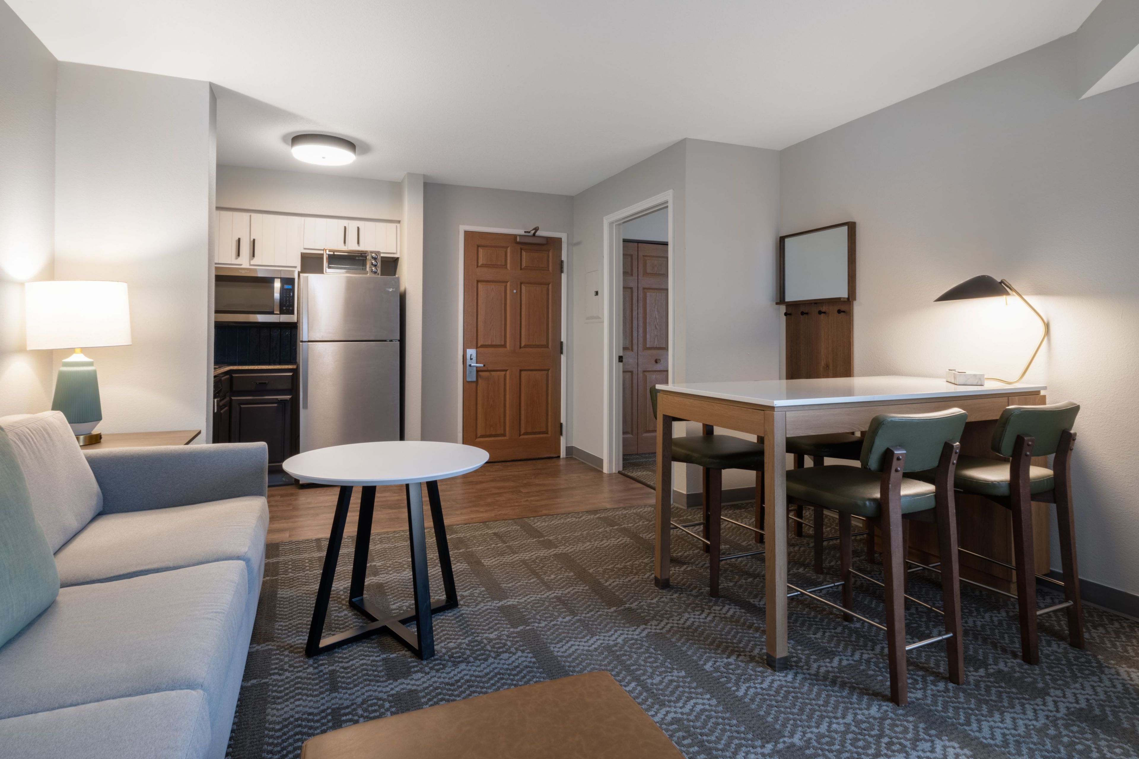 A compact living space with a kitchenette, a dining area with a table and chairs, a sofa, and a lamp.
