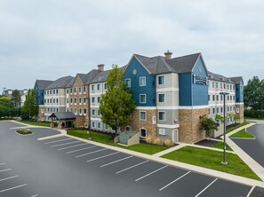 Et hotel i flere etager med en stenfassade, blå og grå ydre og en parkeringsplads foran.
